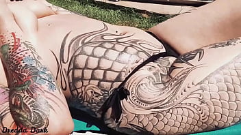 Tattooed horny brunette with big boobs sunbathing in the yard and rubbing sunscreen on her tits
