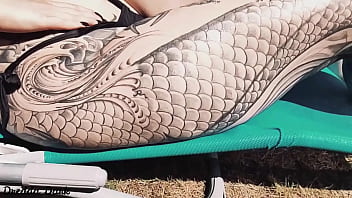 Tattooed horny brunette with big boobs sunbathing in the yard and rubbing sunscreen on her tits