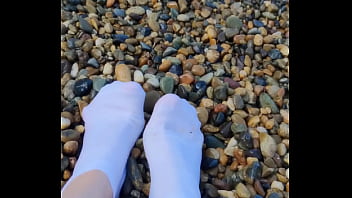 Playing with my feet in white socks with pebbles on the beach