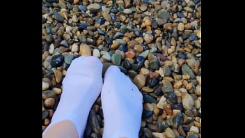 Playing with my feet in white socks with pebbles on the beach