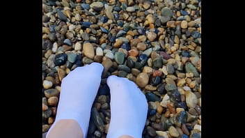 Playing with my feet in white socks with pebbles on the beach
