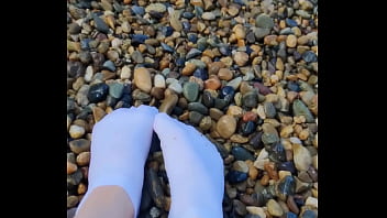 Playing with my feet in white socks with pebbles on the beach