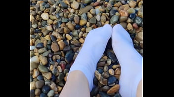 Playing with my feet in white socks with pebbles on the beach