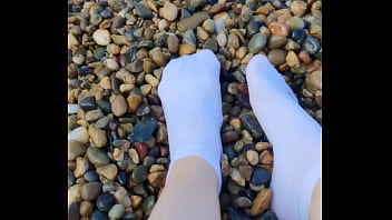 Playing with my feet in white socks with pebbles on the beach