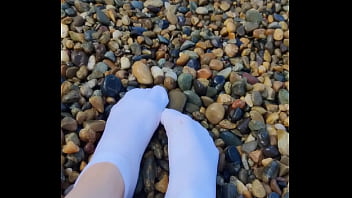 Playing with my feet in white socks with pebbles on the beach