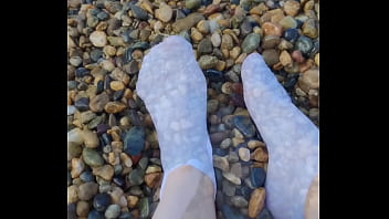 Playing with my feet in white socks with pebbles on the beach