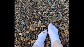 Playing with my feet in white socks with pebbles on the beach