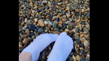 Playing with my feet in white socks with pebbles on the beach