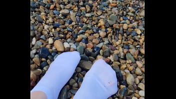 Playing with my feet in white socks with pebbles on the beach